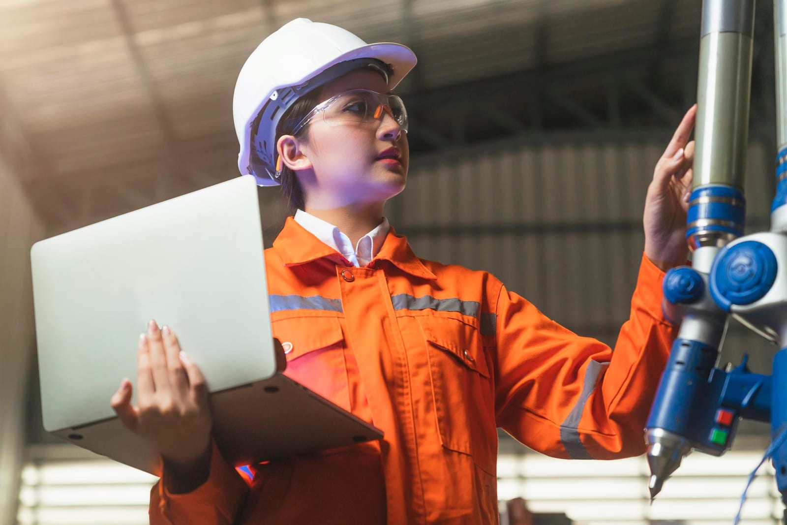 Trabalhador com capacete amarelo e colete de segurança usando um tablet perto de tanques industriais